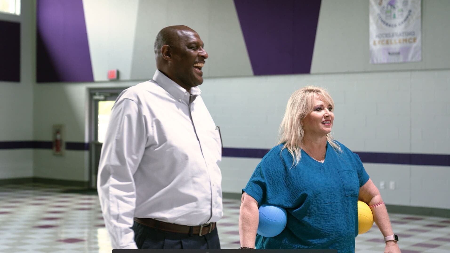 Two teachers standing in a school gym and smiling.