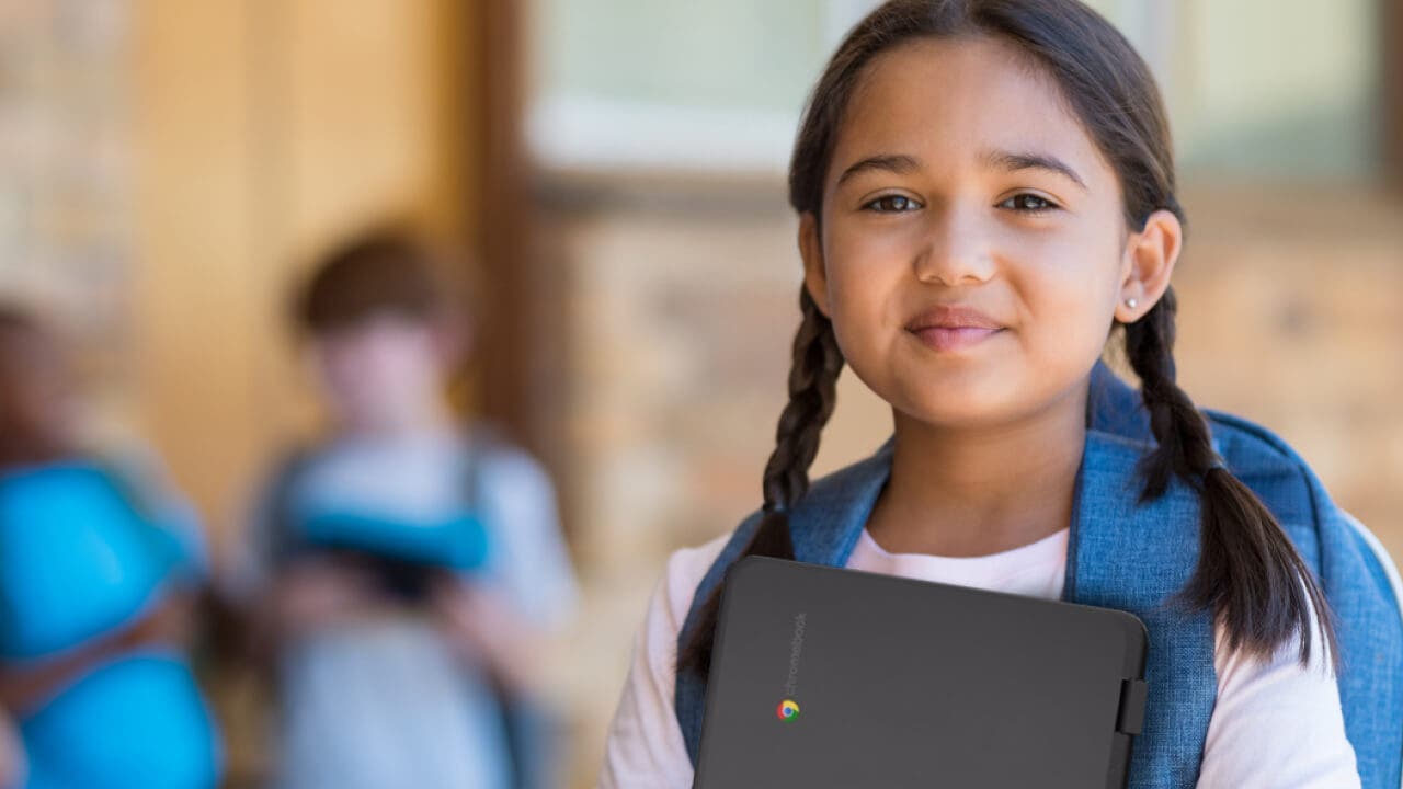 young student smiling and holding a chomebook in her arms